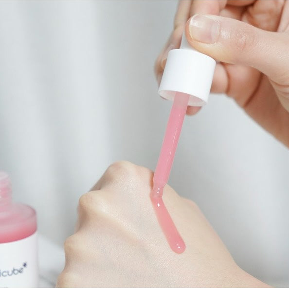 Hand holding a pink liquid from a white bottle with a pump against a light gray background