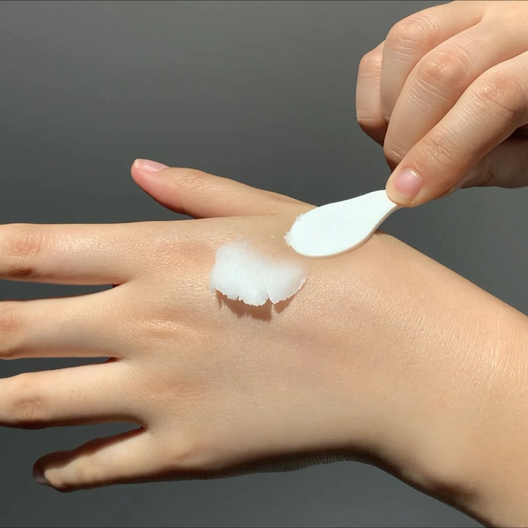 Hand applying white cream to another hand against a dark background